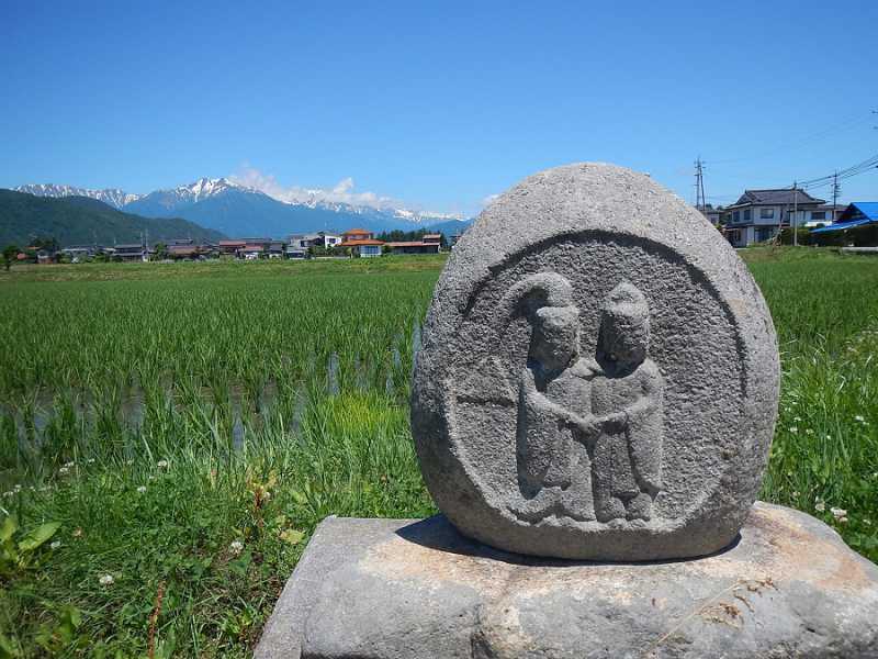 水がはられた田園風景と残雪の北アルプス、道祖神